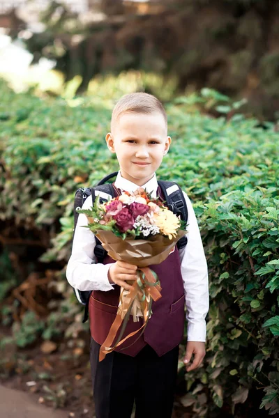 Kleine jongen met bloemen in een hand ga naar school. — Stockfoto
