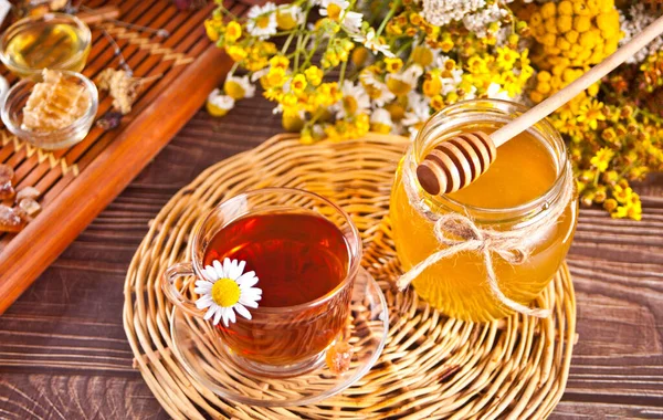 Taza de té de manzanilla con miel en frasco y flores silvestres en el fondo —  Fotos de Stock