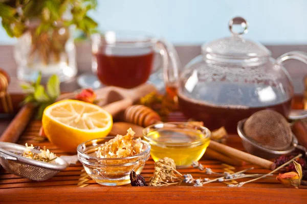 Honing en honingraat in kleine kommen. Theepot en kopje thee op de achtergrond. — Stockfoto
