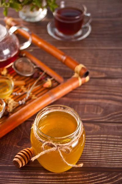 Miel en frasco y panal en tazones pequeños. Tetera y taza de té en el fondo. —  Fotos de Stock