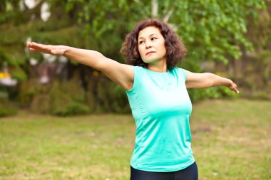 Orta yaşlı, aktif bir kadın parkta egzersiz yapıyor.