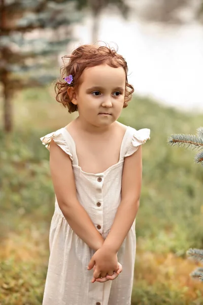Mała szczęśliwa dziewczynka stoi w pobliżu stawu, jeziora lub rzeki. Letnie życie na wsi. — Zdjęcie stockowe