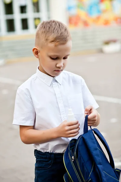 Pojken satte rengöringsmedel eller desinfektionsmedel spray för att desinficera händerna i skolväskan. Karantän för Coronavirus, koncept för förebyggande av pandemier. — Stockfoto