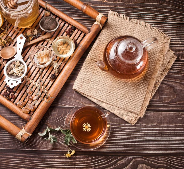 Xícara de chá de ervas com bule e bandeja de madeira com várias ervas secas. Vista superior — Fotografia de Stock