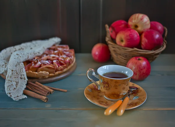 Äppelpaj, korg med äpplen och kopp te på trä bordet — Stockfoto