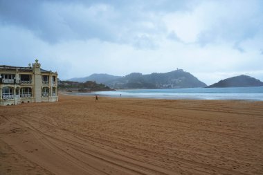 Kışın yağmurlu bir gününde boş bir sahilde yürüyen bir adam.