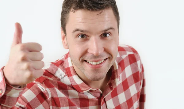 Smiling young man in hipster shirt showing thumb up and standing against white background — Stock Photo, Image