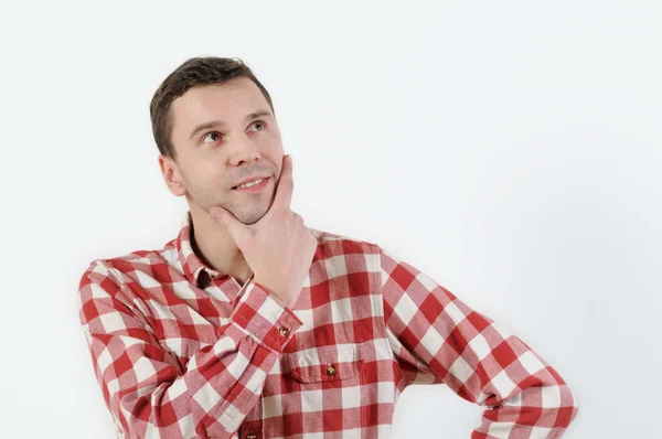 Thoughtful young man in hipster shirt holding hand on chin and standing against white background — Stock Photo, Image