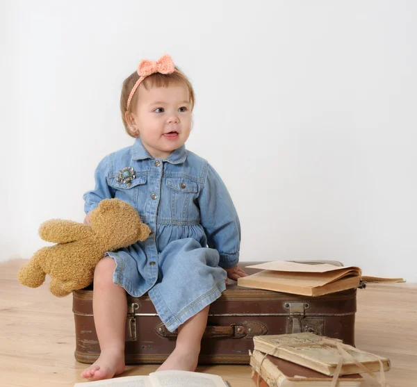 Little girl sitting on suitcase near book — Stock Photo, Image