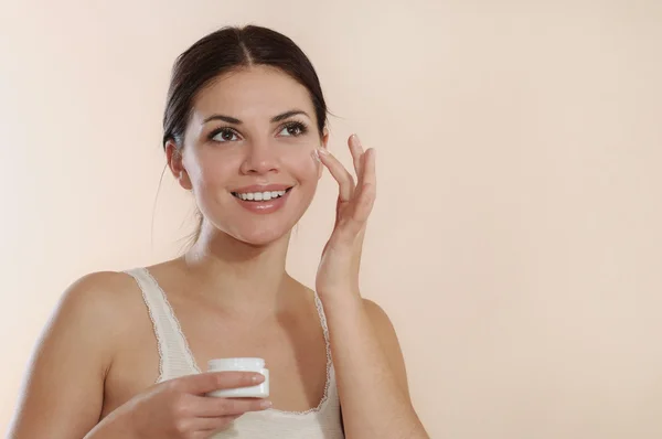 Smiling young woman applying face cream — Stock Photo, Image