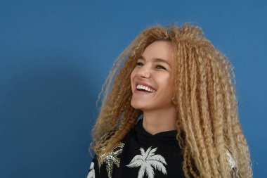 Mavi arka planda sarı kıvırcık saçlı güzel bir kadının portresi. Mutlu yaşam tarzı konsepti.