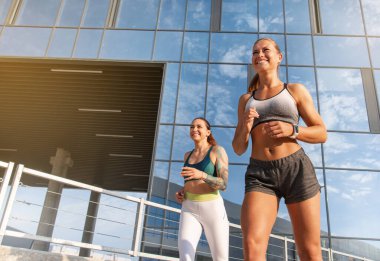 İki kadın güneş batarken şehirde koşu yaparak egzersiz yapıyor. Sağlıklı yaşam tarzı kavramı.