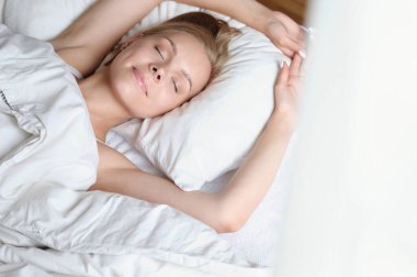 Güzel sarışın bir kadın sabah beyaz bir yatakta uyanıyor. Kişisel bakım yaşam tarzı kavramı