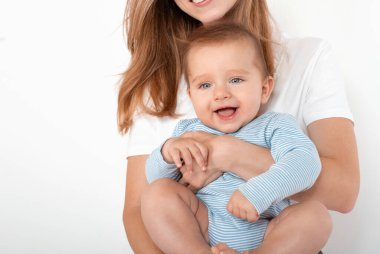 Anne beyaz arka planda güzel mavi gözleri olan sevimli, mutlu bir oğlan çocuğu tutuyor. Mutlu çocukluk ve annelik kavramı.