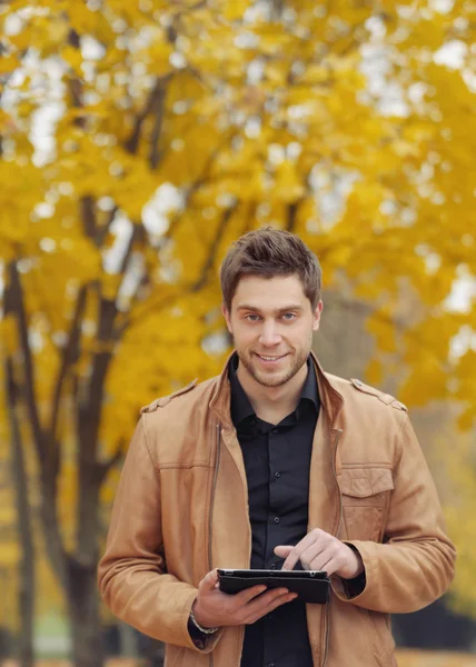 Jovem elegante atraente usando um touchpad no parque de outono — Fotografia de Stock