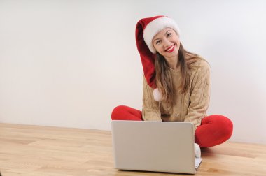Santa şapka ararken güzel genç kadın online için sunar.