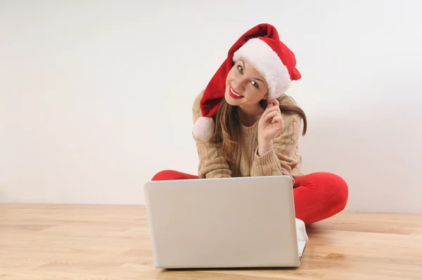 Hermosa joven sonriente en santa hat buscando en línea pres —  Fotos de Stock