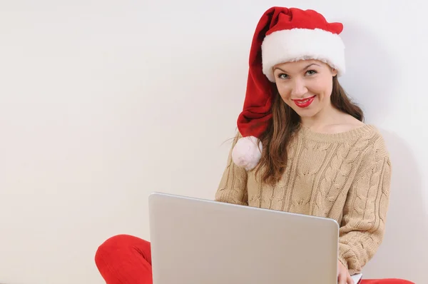 Bella giovane donna in cappello di Babbo Natale seduto sul pavimento con non — Foto Stock
