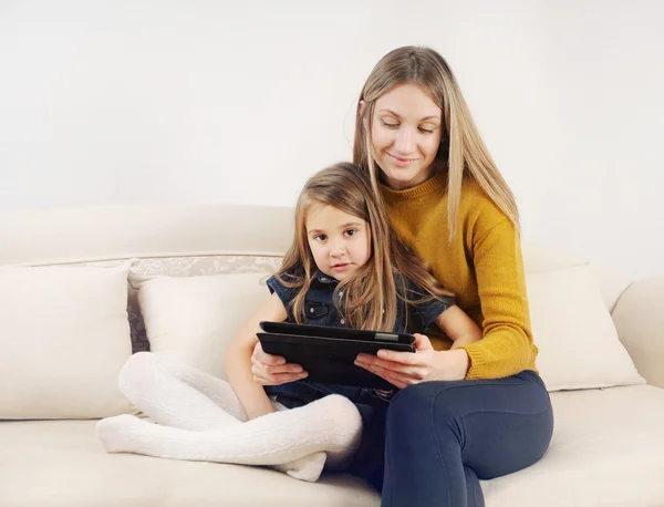 little girl with her mother using tablet device on the sofa at h