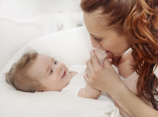 Feliz madre cariñosa besando pequeños dedos de su lindo bebé niño —  Fotos de Stock