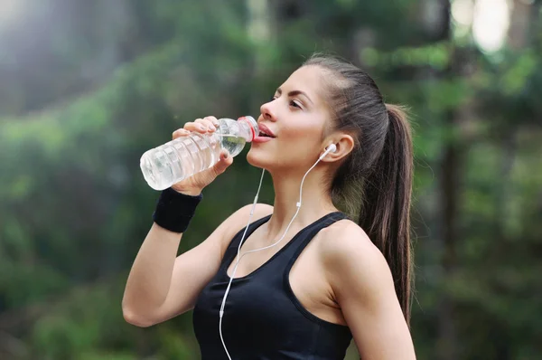 ヘッドフォンで水を飲むと健康的なライフ スタイルのスポーティな女性 ストックフォト