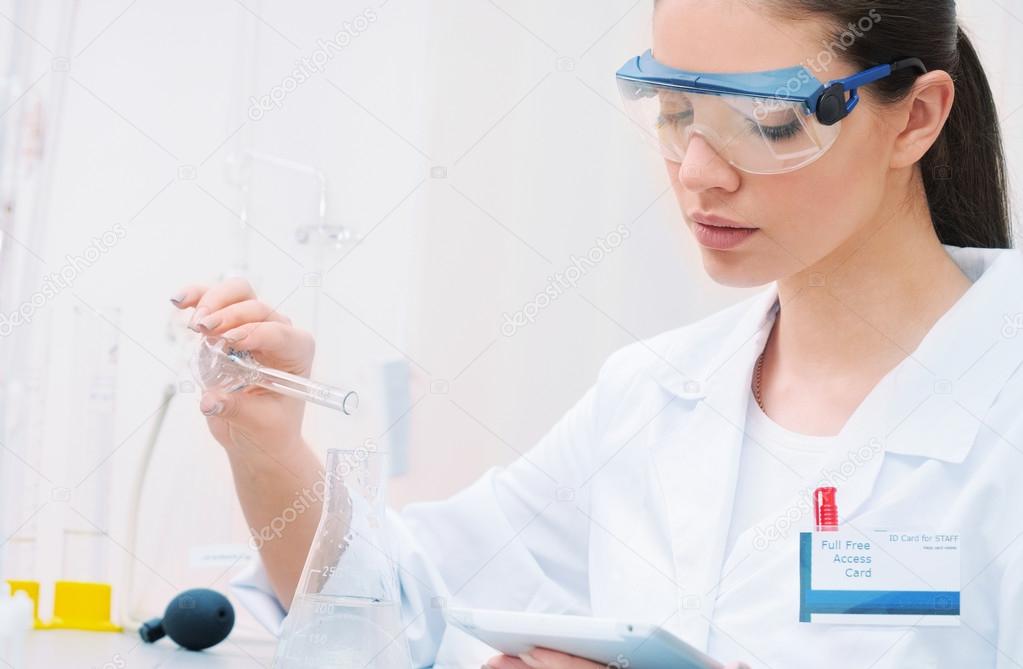 young woman scientist in glasses working and observing liquid at