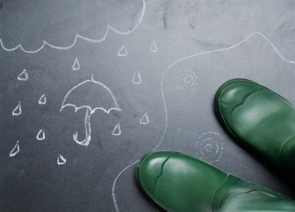 Rubber boots with drawing of rainy day on the blackboard from th — Stock Photo, Image