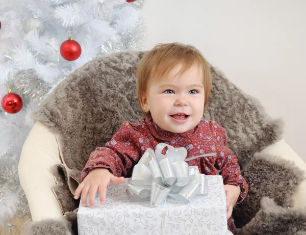 Little baby girl with big gift in hands near Christmas tree — Zdjęcie stockowe