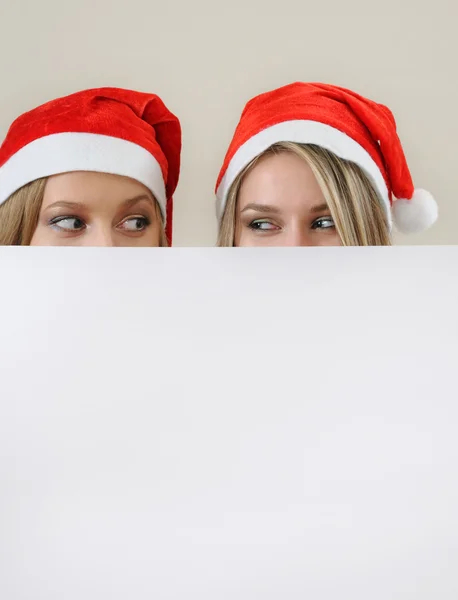 Tho happy girl in santa hat hiding behind a empty blank banner w — Zdjęcie stockowe