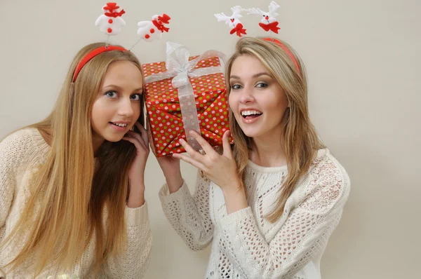 Dos mujeres felices sostienen cerca de la cabeza y escuchan caja de regalo —  Fotos de Stock