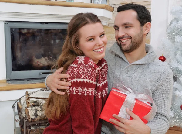 Uśmiechający się młodego człowieka ogarnia jego dziewczyną i dając jej Christm — Zdjęcie stockowe