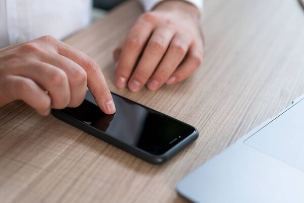 Closeup of male office manager typing on black phone screen, lying on wooden office table desk. Man hands with phone searching for information, no face. Concept of phone