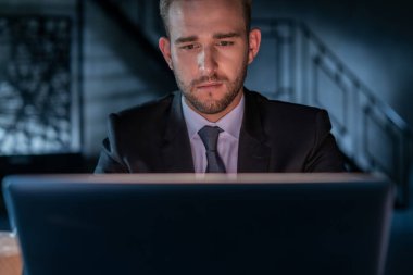 Siyah takım elbiseli yorgun işadamı, gece geç saatlere kadar ofiste çalışıyor. Ofis müdürü karanlık ofis odasının arka planında laptopla çalışıyor. Aşırı çalışma kavramı