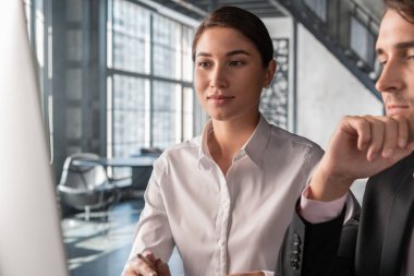 Siyah takım elbiseli erkek ortağı olan kadın ofis müdürü iş hakkında konuşuyor. Ofisteki iş ortakları bilgisayar ekranına, ofis içi geçmişine, takım çalışması kavramına bakıyorlar.