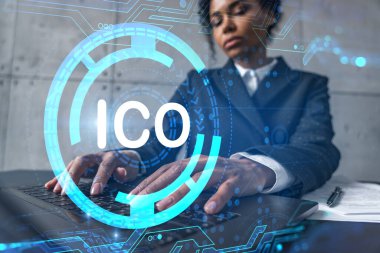 Yeni bir proje için modern ofiste dizüstü bilgisayarla yazı yazan bir iş kadını. ICO simgesi hologram çiziyor. Çifte maruziyet. Başarı kavramı.