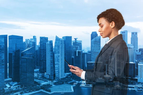 Привлекательная чернокожая афроамериканская деловая женщина в костюме, использующая смартфон и думающая, как решить проблему, новые карьерные возможности, MBA. Сингапур на заднем плане. Двойное воздействие. — стоковое фото