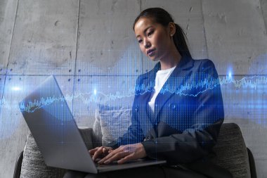 Yeni bir proje için modern ofiste dizüstü bilgisayarla yazı yazan bir iş kadını. Finansal pazar grafiği hologram çiziyor. Çifte maruziyet. Başarı kavramı.