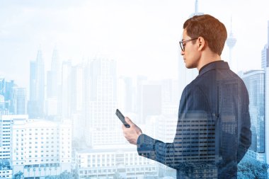 Takım elbiseli ve gözlüklü genç yakışıklı işadamı telefonla sorunu nasıl halledeceğini düşünüyor. Yeni kariyer fırsatları, işletme mastırı. Kuala Lumpur arka planda. Çift pozlama.