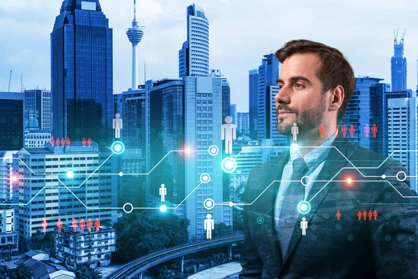 Handsome Caucasian HR director at international company is thinking about efficient strategy to recruit highly qualified specialists. Social media marketing hologram icons over Kuala Lumpur background