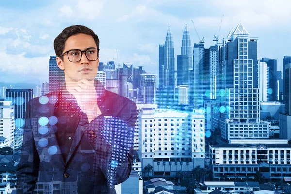 Handsome eastern HR director at international company thinking about efficient strategy to recruit highly qualified specialists. Social media and marketing hologram icons over Kuala Lumpur background