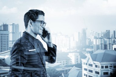 Takım elbiseli, gözlüklü, telefonla konuşan ve Kuala Lumpur şehri manzarasına bakan başarılı yakışıklı girişimci. Sorun çözme danışmanlığı kavramı. KL gökdelenleri. Çift pozlama.