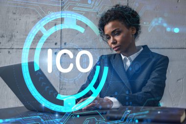 Yeni bir proje için modern ofiste dizüstü bilgisayarla yazı yazan bir iş kadını. ICO simgesi hologram çiziyor. Çifte maruziyet. Başarı kavramı.