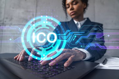 Yeni bir proje için modern ofiste dizüstü bilgisayarla yazı yazan bir iş kadını. ICO simgesi hologram çiziyor. Çifte maruziyet. Başarı kavramı.