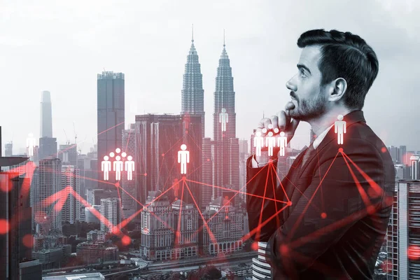 Handsome Caucasian HR director at international company is thinking about efficient strategy to recruit highly qualified specialists. Social media marketing hologram icons over Kuala Lumpur background