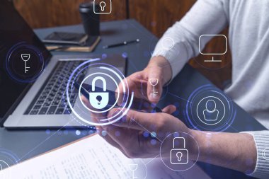 Bir programcı, bir siber güvenliği hacker saldırılarından korumak ve müşterilerinin gizli verilerini kaydetmek için akıllı telefonuyla internete giriyor. Yazan ellerin üzerine asma kilit hologramı simgeleri.