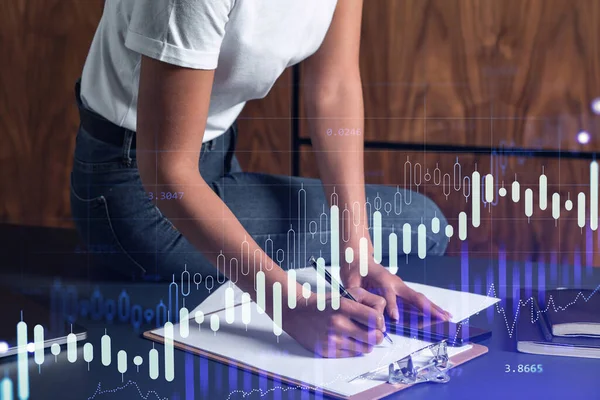 A woman trader in casual wear writing down some quotes to research stock market trends using smart phone for right investment. Wealth management concept. Hologram Forex chart over close up shot.