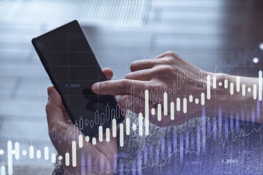 Elinde akıllı bir telefon tutan tüccar doğru yatırım çözümlerine ulaşmak için borsayı araştırıyor. İnternet ticareti ve zenginlik yönetimi kavramı. Hologram Forex grafiği yakın çekim üzerine.