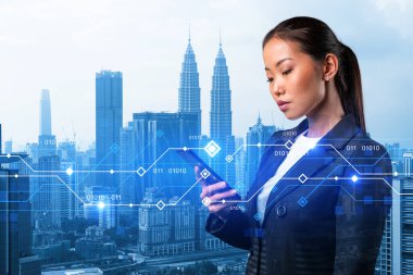 Akıllı telefondan interneti araştırarak yeni teknolojik yaklaşımlar kullanarak ticarette muazzam bir büyüme sağlamaya çalışan çekici Asyalı iş kadını. Kuala Lumpur üzerinde teknik hologram simgeleri