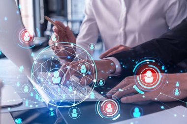İki İK uzmanı, uluslararası danışmanlık şirketindeki stajyerlik programını hızlandırmak için dizüstü bilgisayar kullanarak işe alım pazarını analiz ediyor. Sosyal ağ hologram simgeleri.