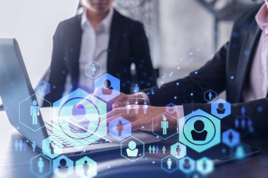 İki İK uzmanı, uluslararası danışmanlık şirketindeki stajyerlik programını hızlandırmak için dizüstü bilgisayar kullanarak işe alım pazarını analiz ediyor. Sosyal ağ hologram simgeleri.